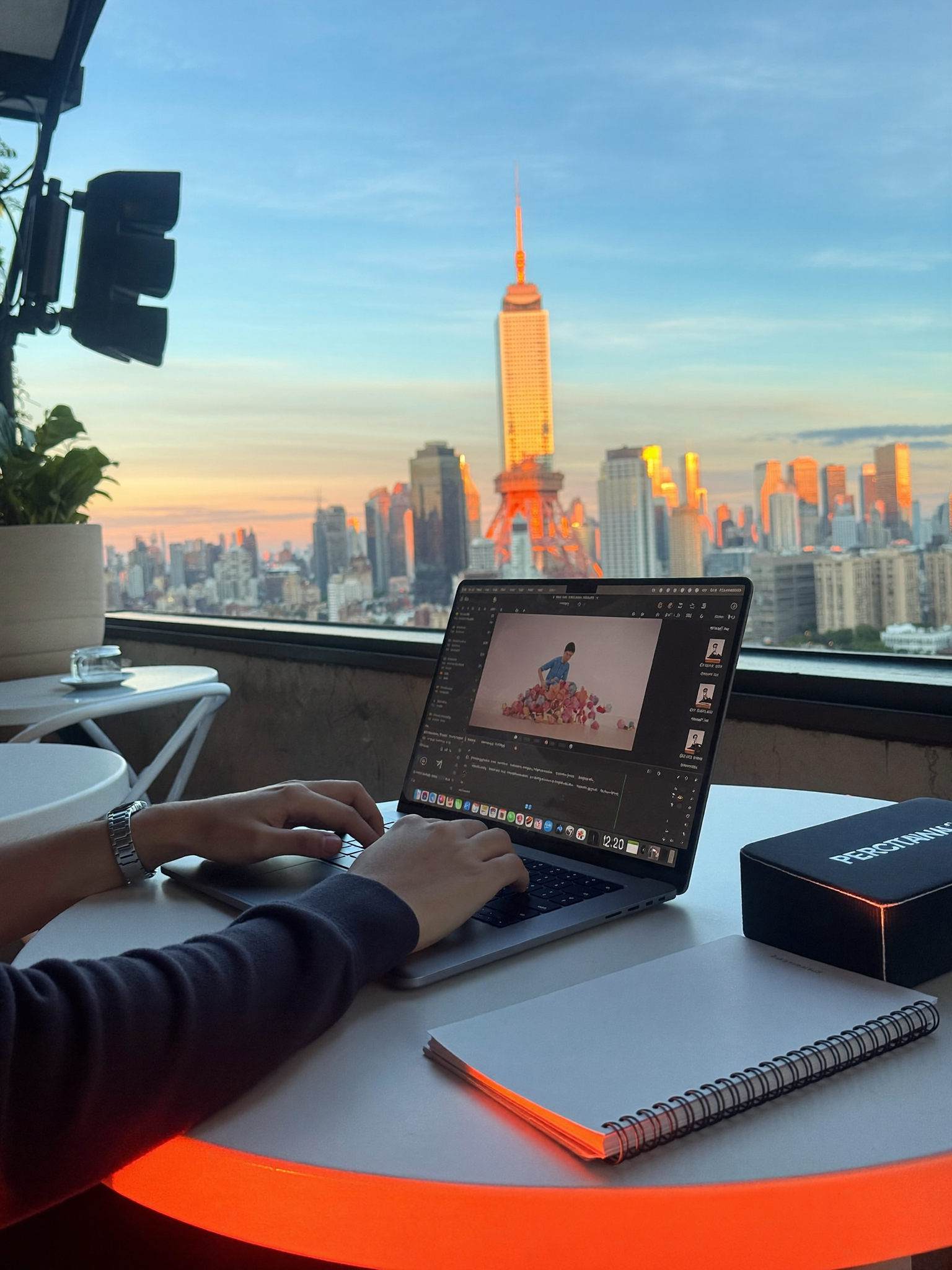 A creator editing video at a rooftop cafe with the morning skyline behind